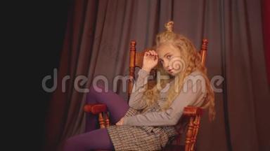 年轻女孩坐在木椅上进行时尚拍照。 时装模特少女在摄影棚的椅子上摆姿势